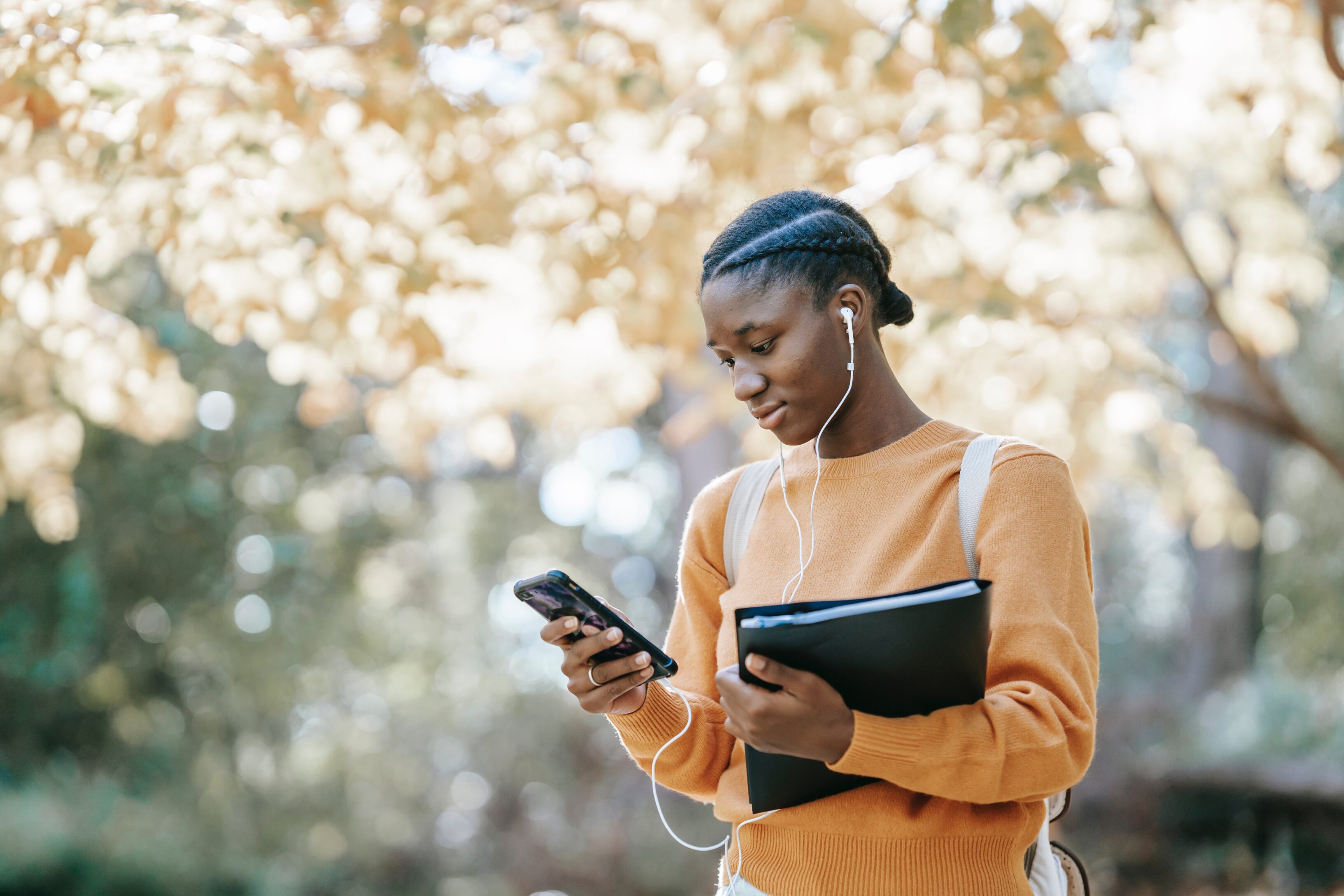 A teenage student holding her books and looking at her phone